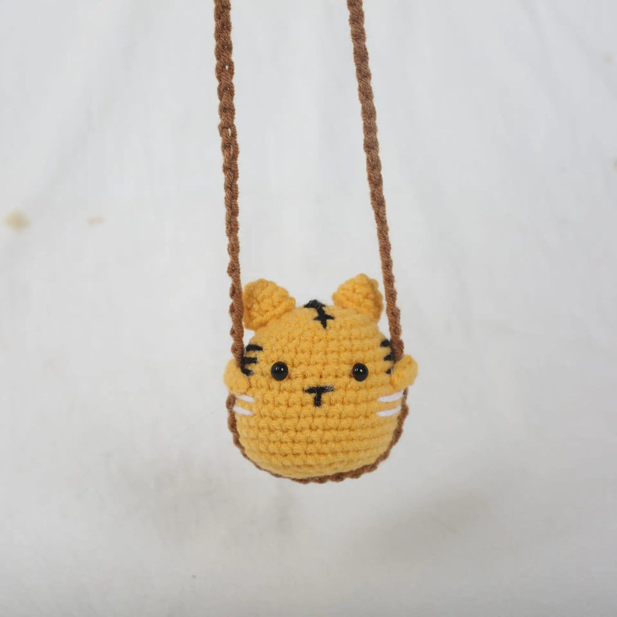 A yellow crochet tiger hanging charm with a brown leather cord.