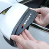 A hand holds a white and black car side mirror rain deflector set with an orange and red Sport logo.