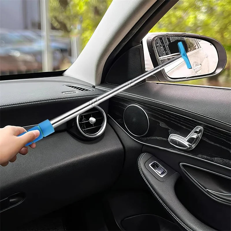 A hand is using a blue universal car and glass cleaning tool to wipe the interior mirror of a car.