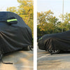 A black all-weather waterproof UV car cover is shown covering a vehicle outdoors.