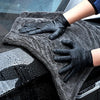 Hands wearing black gloves are cleaning a car window with a gray microfiber cloth.