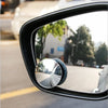 A close-up view of a black car rearview mirror with a circular blind spot camera mounted on it.