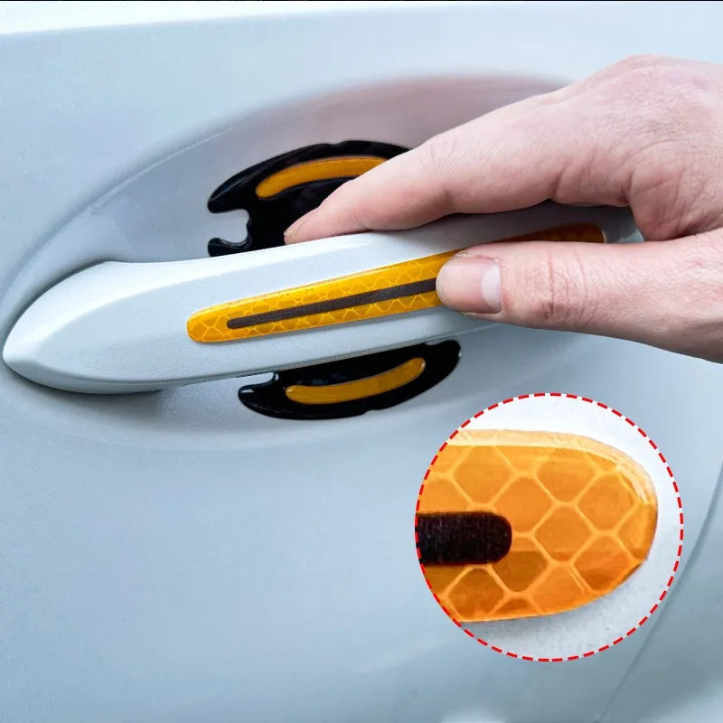 A hand is holding a carbon fiber reflective car door handle protector, showing the orange and black design detail.
