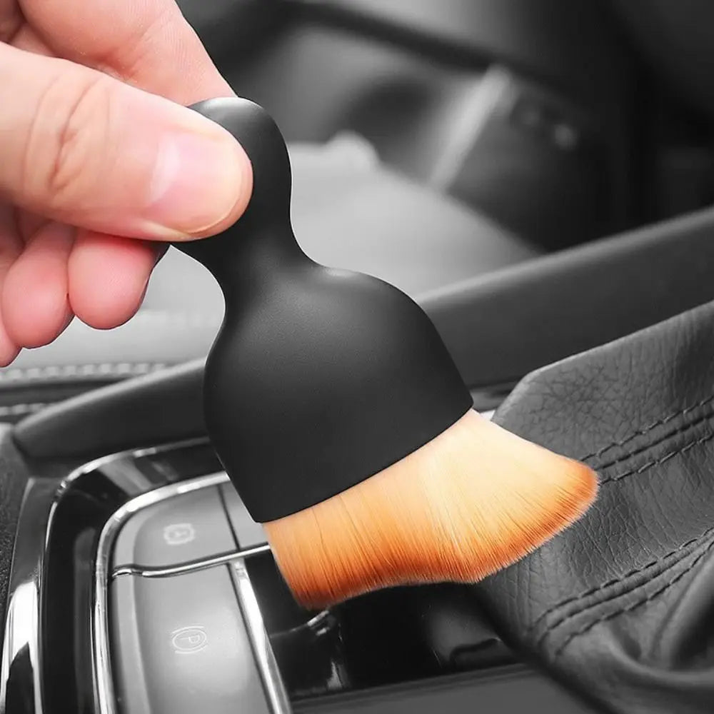 A hand holds a black curved silicone brush used for cleaning car interiors.