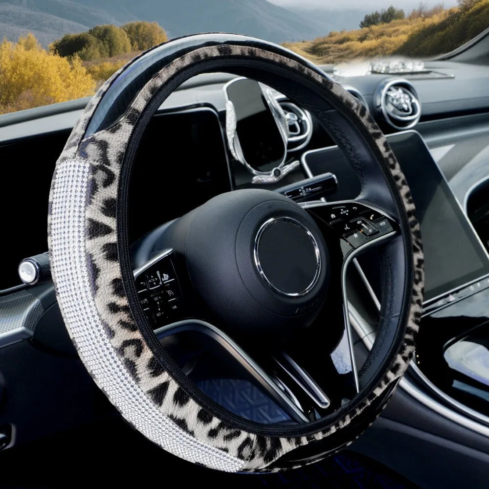 A close-up view of a black steering wheel with a leopard print cover and rhinestone accents inside a car interior.