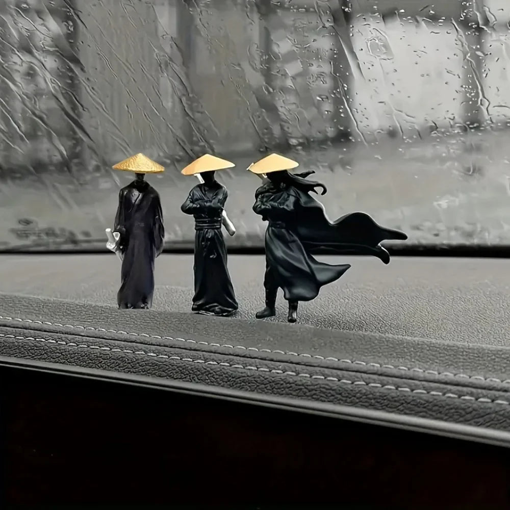 Three miniature samurai statues with golden hats are displayed on a dark surface in a rainy outdoor setting.