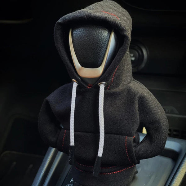 A black Gear Shift Hoodie cover with a hood and drawstring is shown inside a car console.