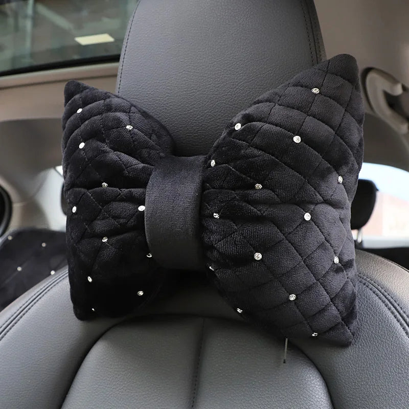 A black diamond rhinestone car neck pillow bow is placed on a gray car seat.
