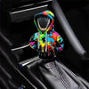 A colorful, abstractly painted knit gear shift cover is shown inside a black car shifter boot.