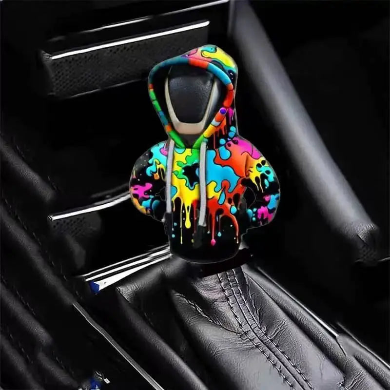 A colorful, abstractly painted knit gear shift cover is shown inside a black car shifter boot.