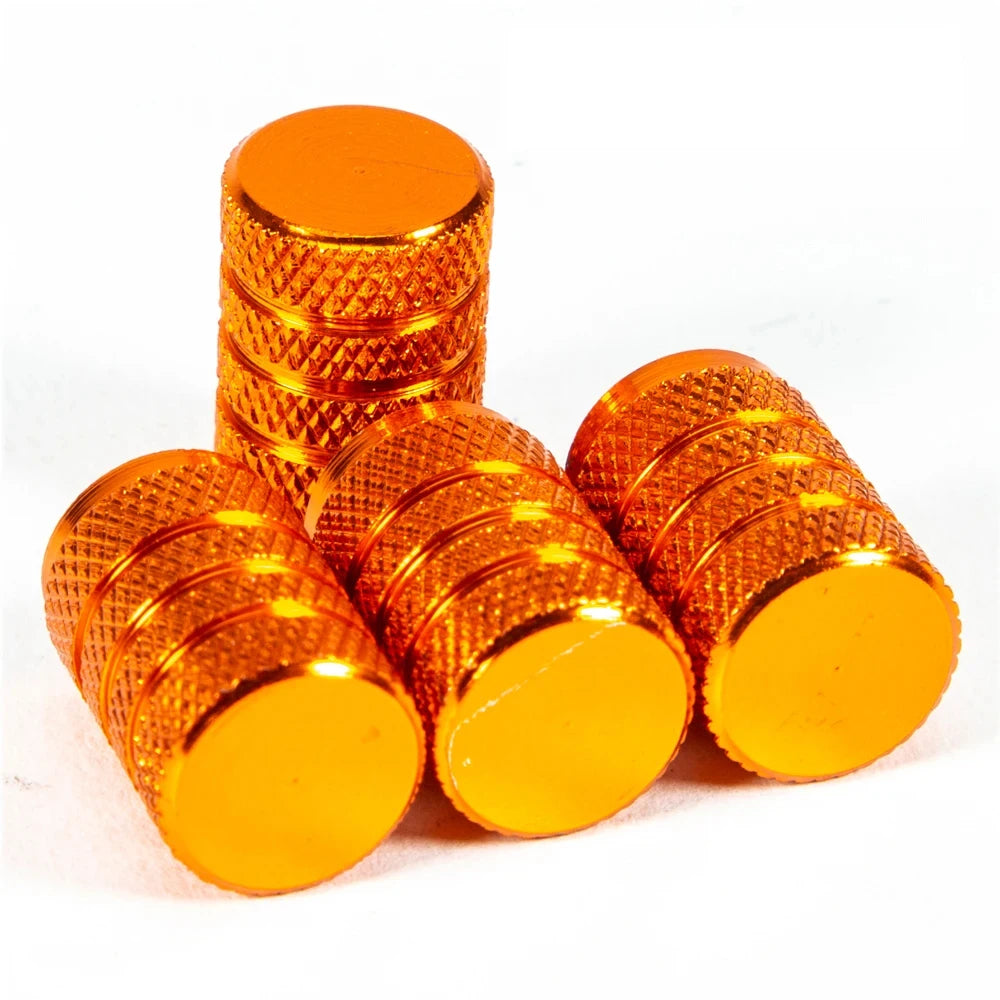 A set of shiny orange aluminum tire valve caps stacked and scattered on a white background.