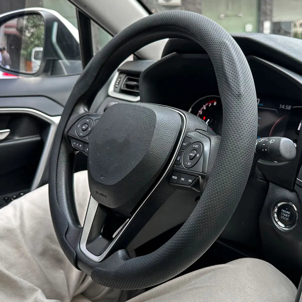 Nahaufnahme eines schwarzen Lenkrads mit Bedienelementen und einer Leder-Lenkradabdeckung im Auto-Innenraum.