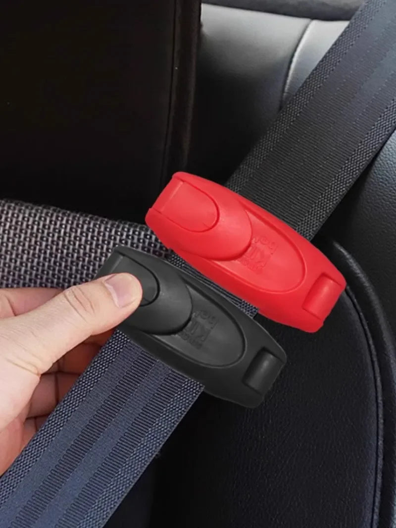 A hand is holding a black seat belt clip and a red adjustment piece on a dark car seat fabric.