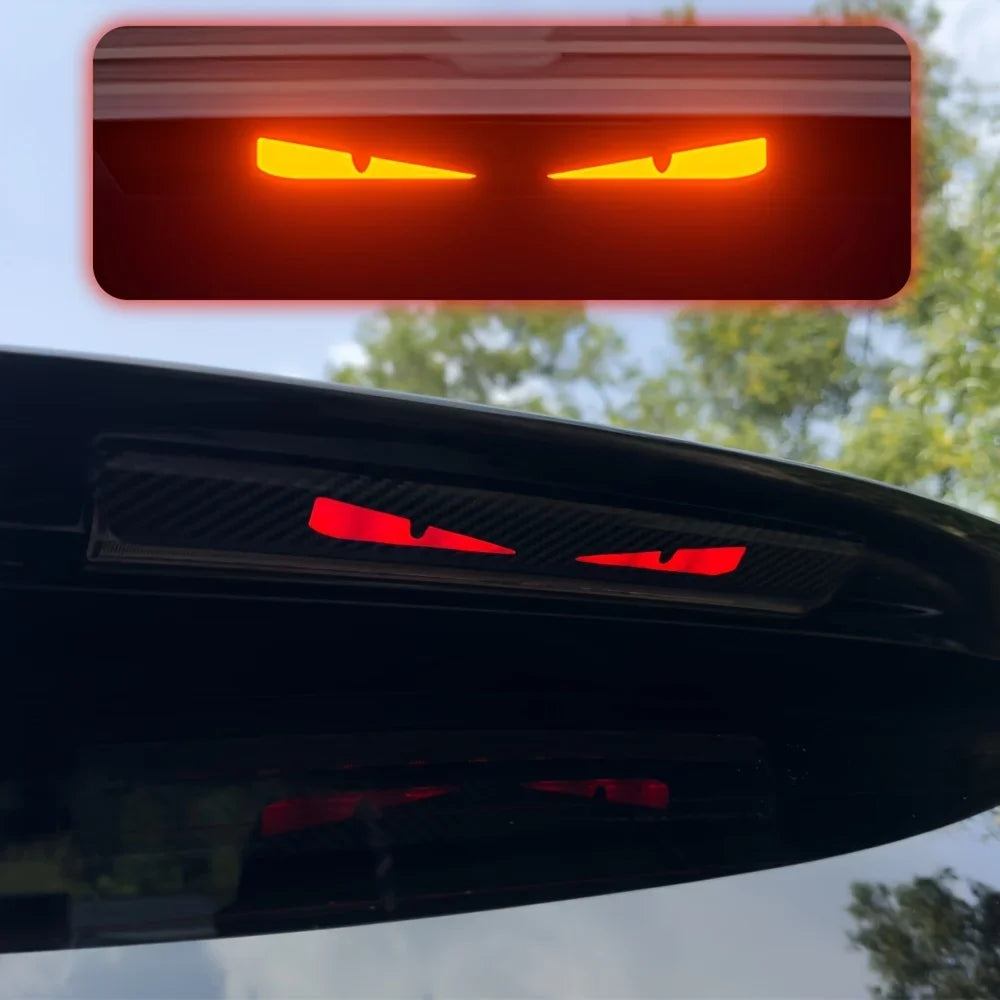 Gros plan d'un autocollant de phares rouge monstre sur l'arrière d'un véhicule noir.