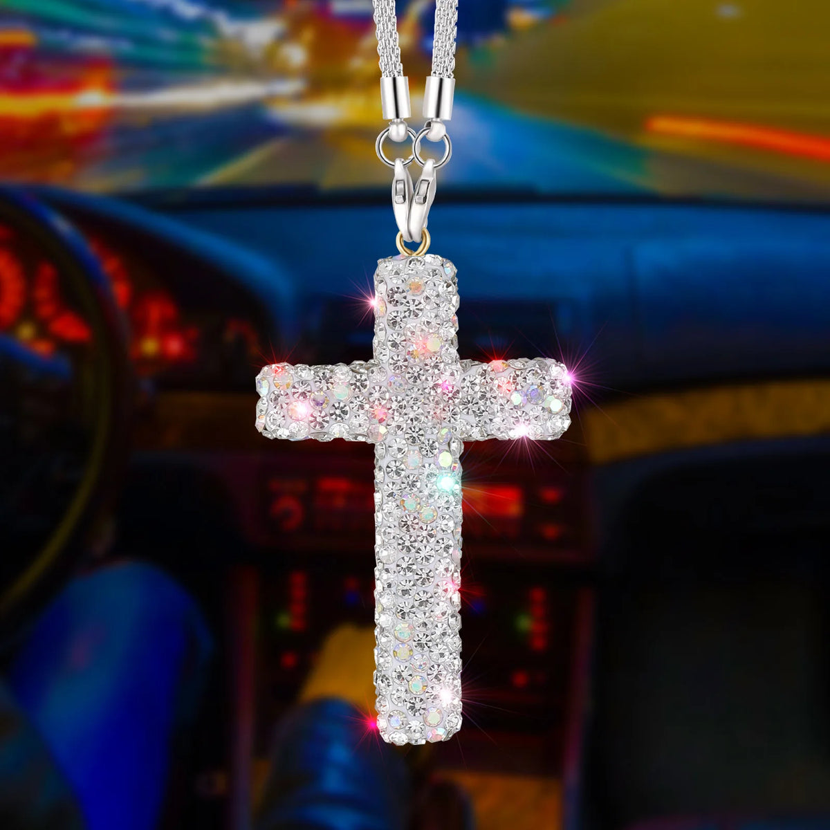 A sparkling silver cross pendant suspended from a chain, displayed against a blurred car interior background.