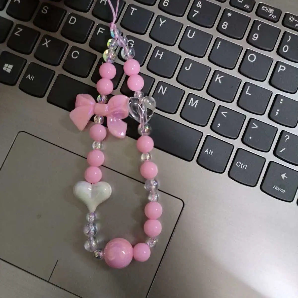 Pink phone anti-loss lanyard with a round bead pendant hanging over a black laptop keyboard