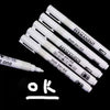 A set of black and white waterproof permanent paint markers arranged diagonally on a dark background.