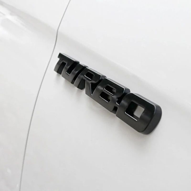 Black three-dimensional metal alloy turbo badge mounted on a white car body.