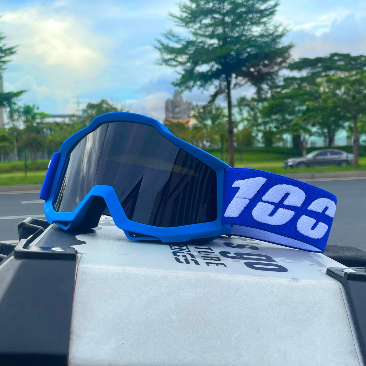 Blue off-road motorcycle goggles with a white '100' logo resting on a dark surface.