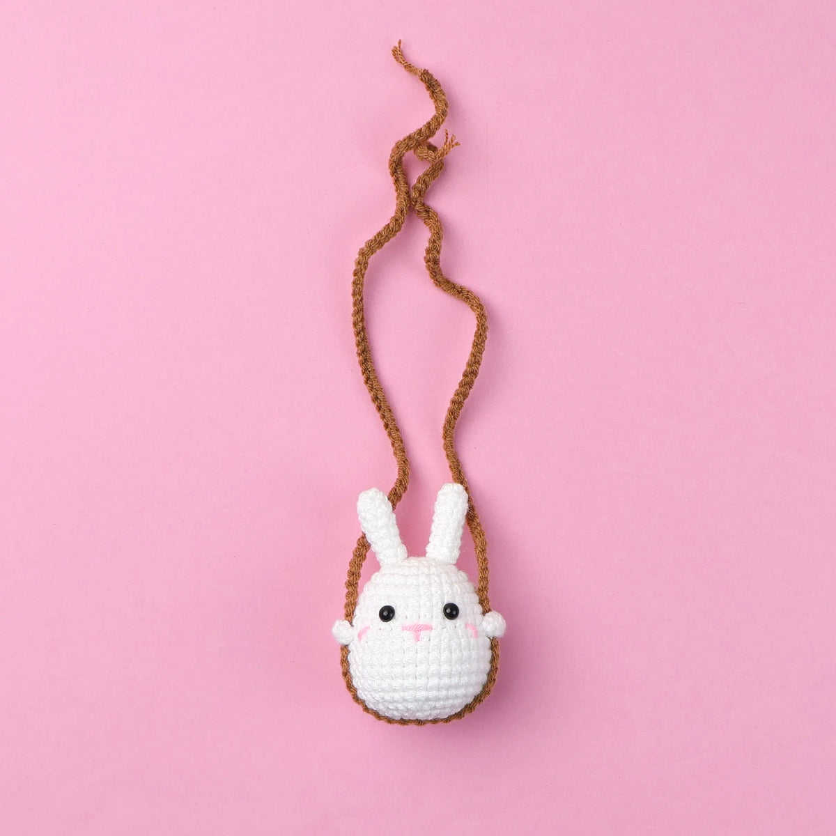 A small white crochet rabbit hanging from a brown string on a pink background.