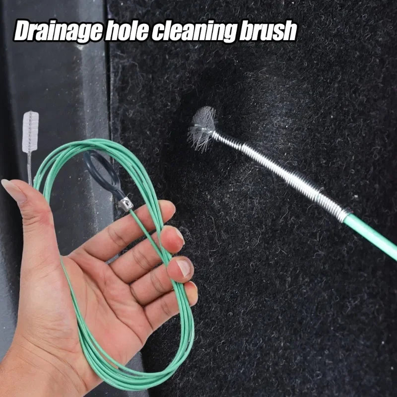 Une main tient une brosse de nettoyage pour évacuation verte à poils de fil contre une surface sombre.