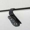 Schwarzer Halter für Sonnenbrillen mit Kristallakzent, montiert auf weißer Oberfläche.