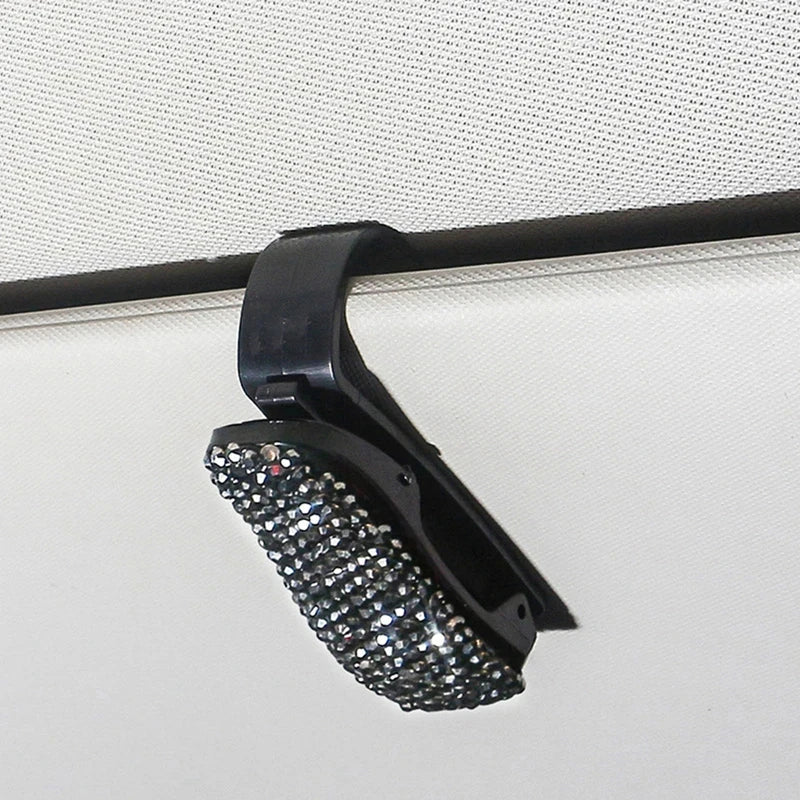 Schwarzer Halter für Sonnenbrillen mit Kristallakzent, montiert auf weißer Oberfläche.