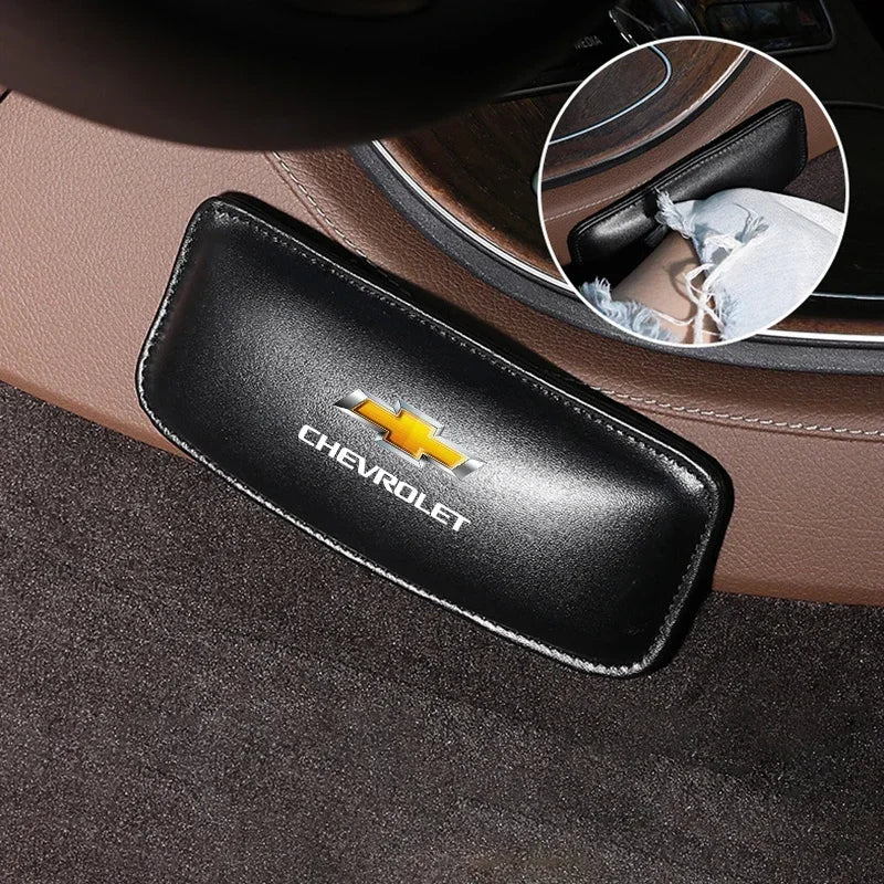 Black leather knee pads for car driving resting on a dark fabric surface.