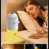 A woman rests her head while a white night light projector casts a warm yellow glow onto her face.