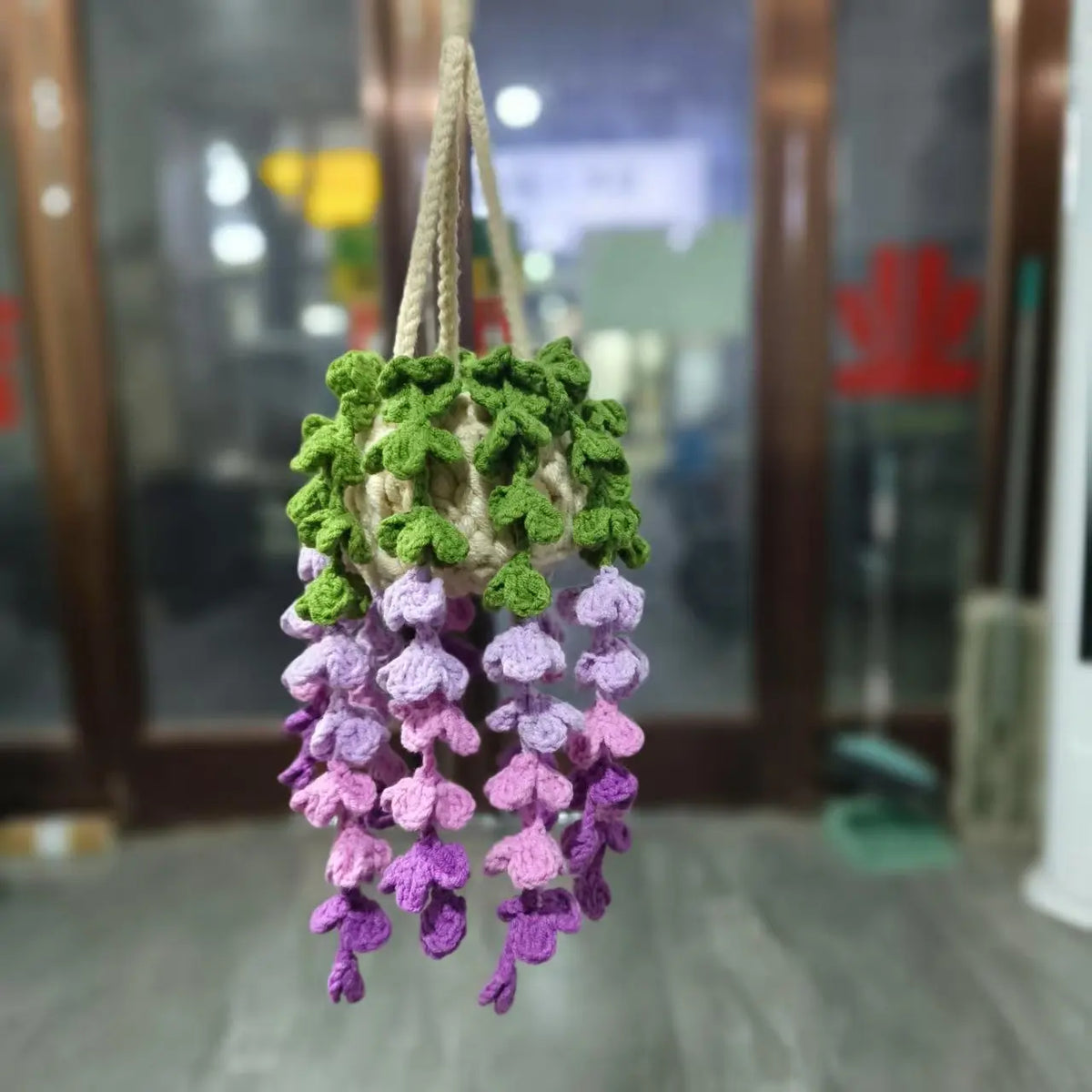 A handmade crochet hanging decor featuring green and purple strawberry-like elements.