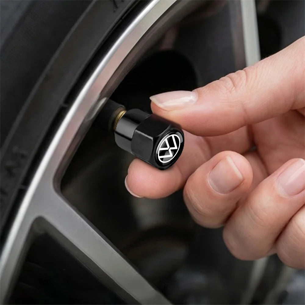 A hand is inserting a black metal tire valve cap into a car wheel rim.