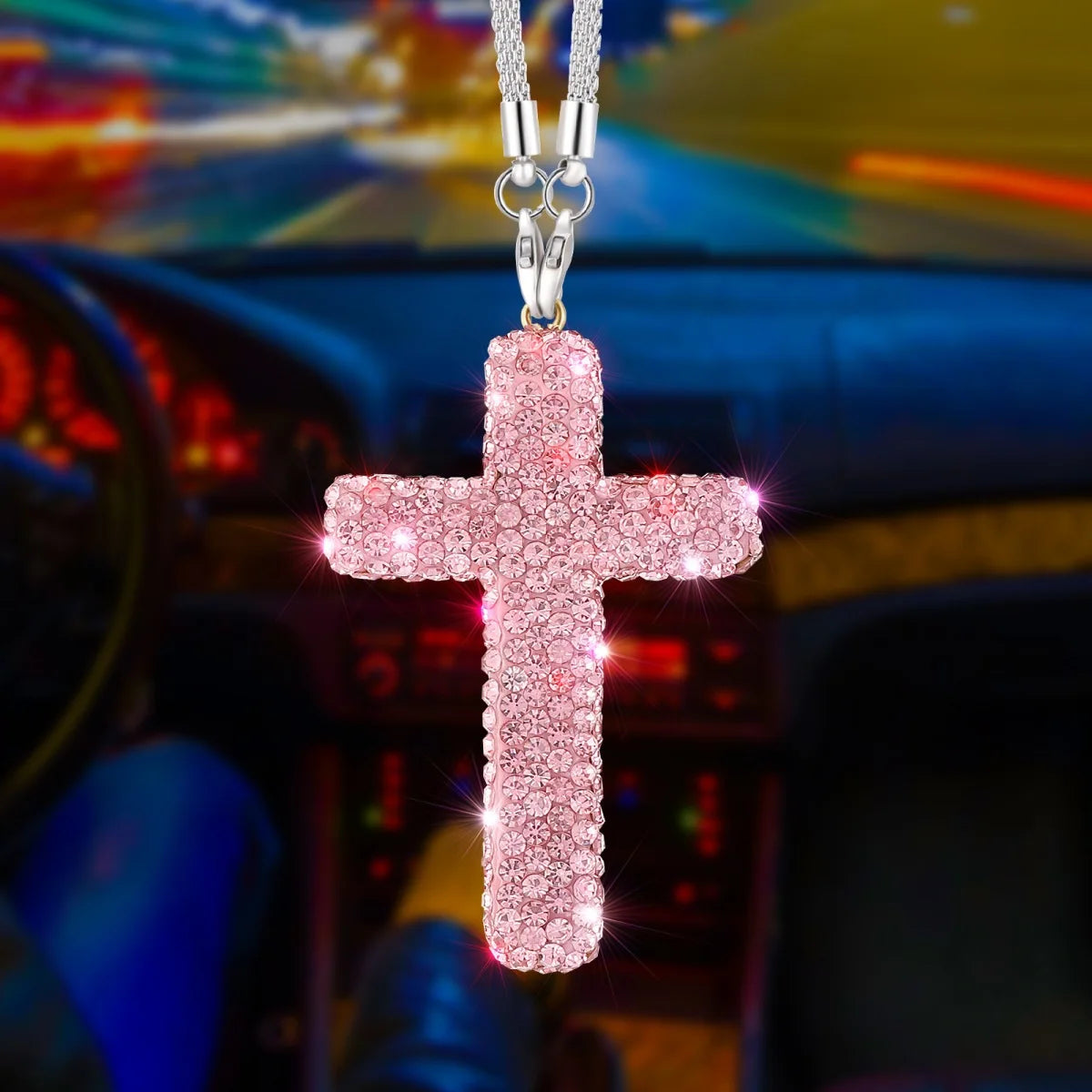 A pink glitter cross pendant on a silver chain hanging in front of a car interior.