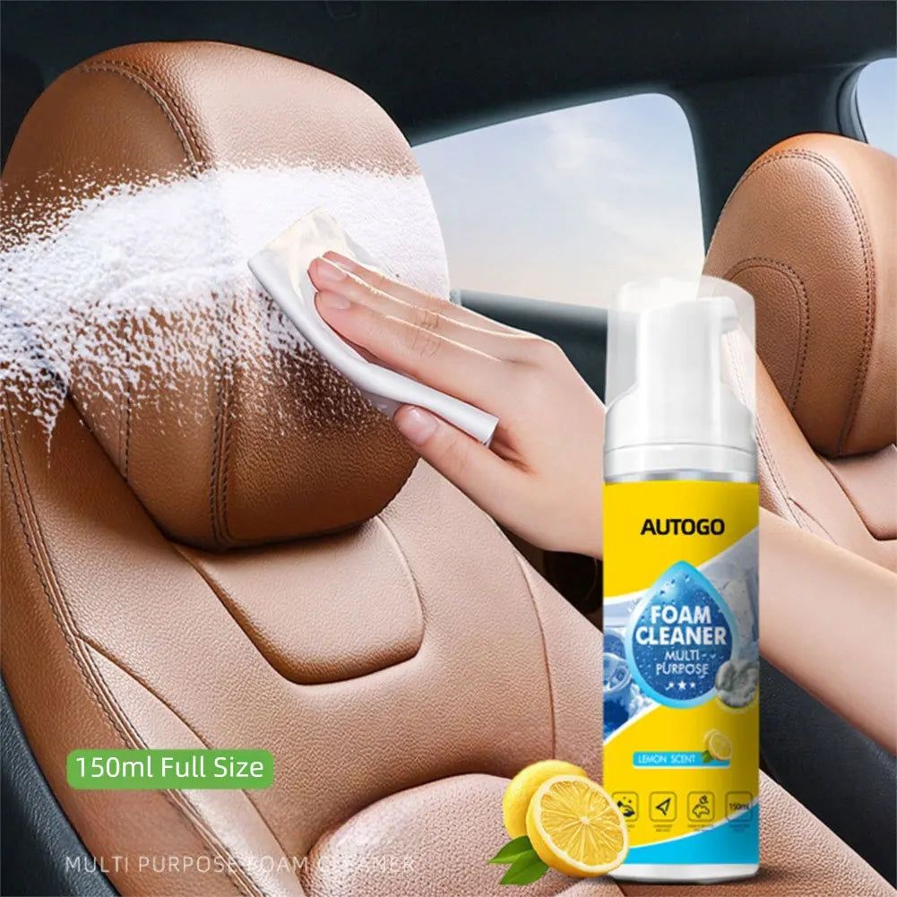 A hand is applying a white foam cleaner to a brown car seat, with the bottle of Autogo foam cleaner visible nearby.