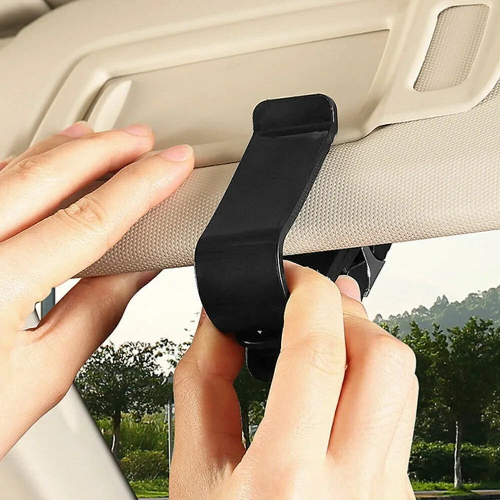 A hand is clipping a black universal car glasses holder clip onto a beige car interior panel.