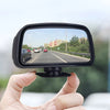 Une main tient un miroir convexe noir montrant une vue d'une route et de bâtiments environnants.