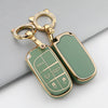 A gold-toned TPU car key case cover with a green insert and a keyring is shown on a gray surface.