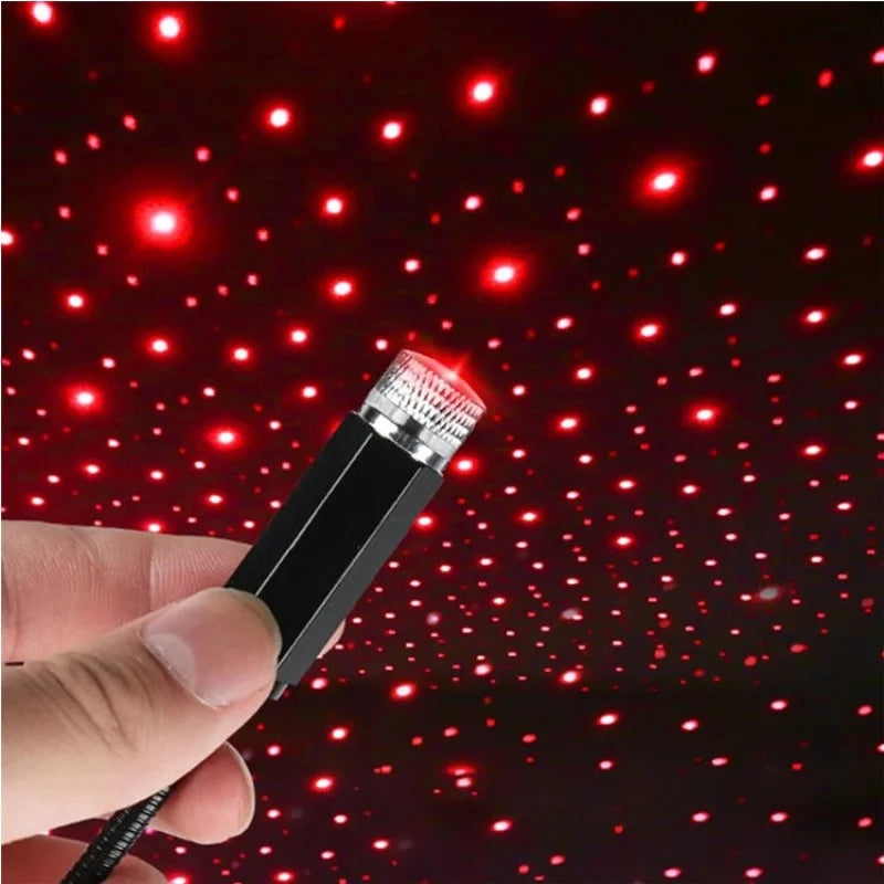 A hand holds a portable LED star projector night light emitting bright red dots against a dark background.