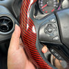A hand is holding a red and black patterned steering wheel booster cover for a car.