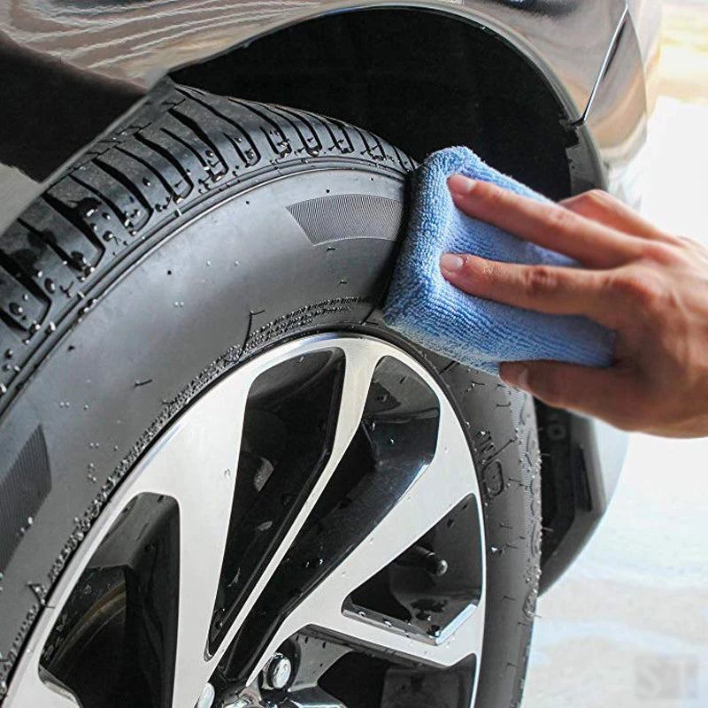 A hand is using a blue microfiber pad to polish the rim of a car wheel.