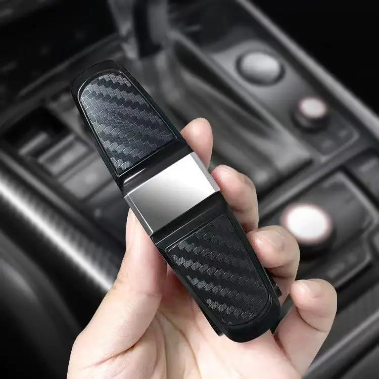 A hand holds a black carbon fiber clip designed to hold sunglasses and eyeglasses in a car