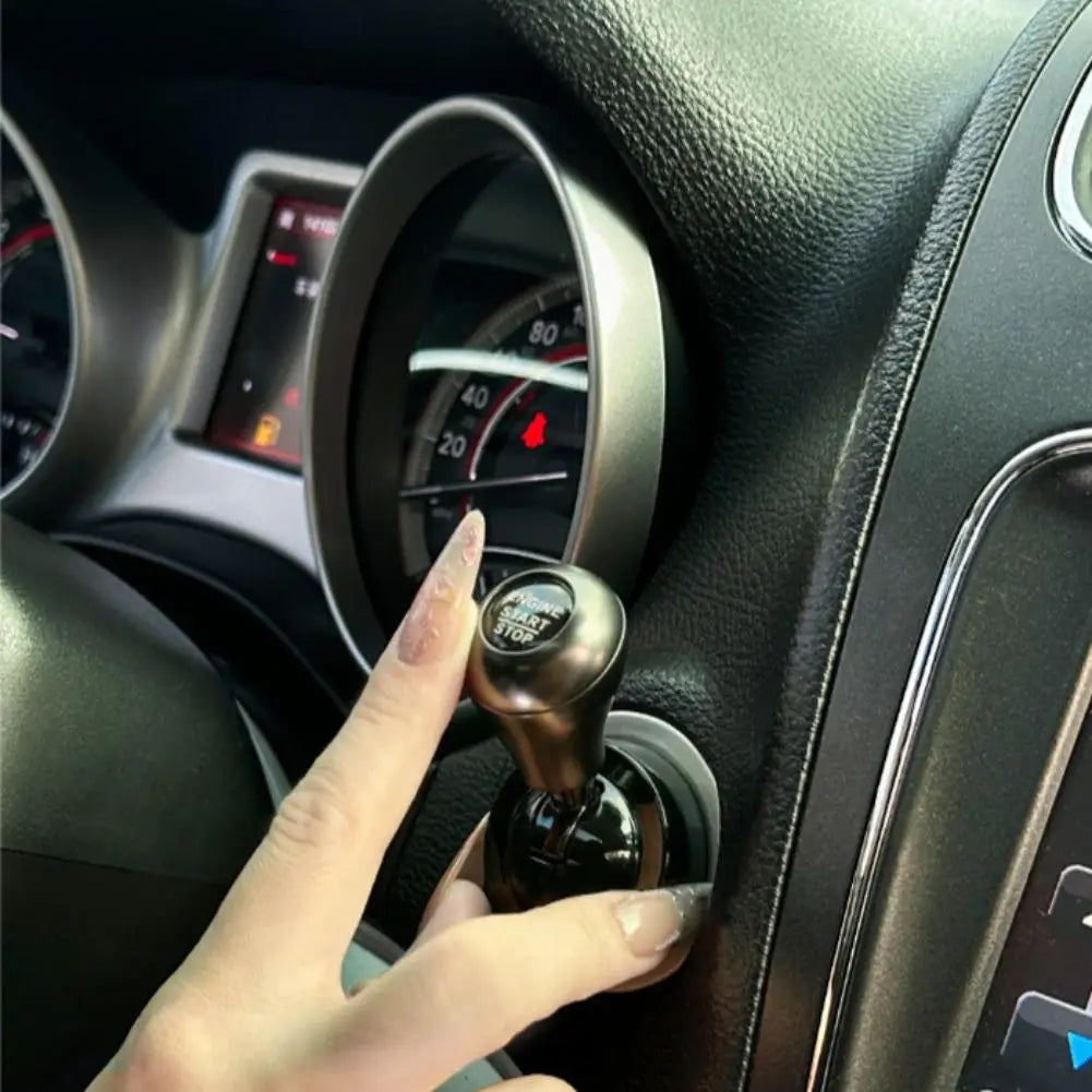 A hand is operating a black metal engine start lever decoration inside a car dashboard.
