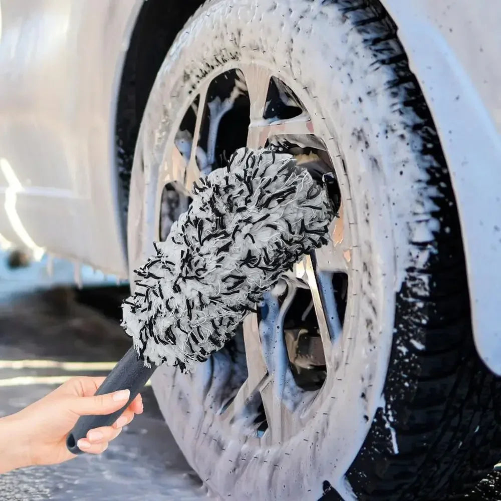 Une main utilise une brosse en microfibre douce pour nettoyer la neige et la saleté d'un jante de voiture.