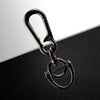 A silver metal key fob with a split ring attached, resting on a black textured surface.