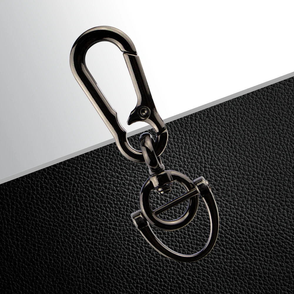 A silver metal key fob with a split ring attached, resting on a black textured surface.
