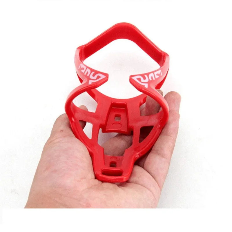 A red plastic bicycle bottle holder rack is shown being held in a hand.