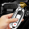A hand holds a silver car key cover with a fingerprint scanner, positioned near a black car.