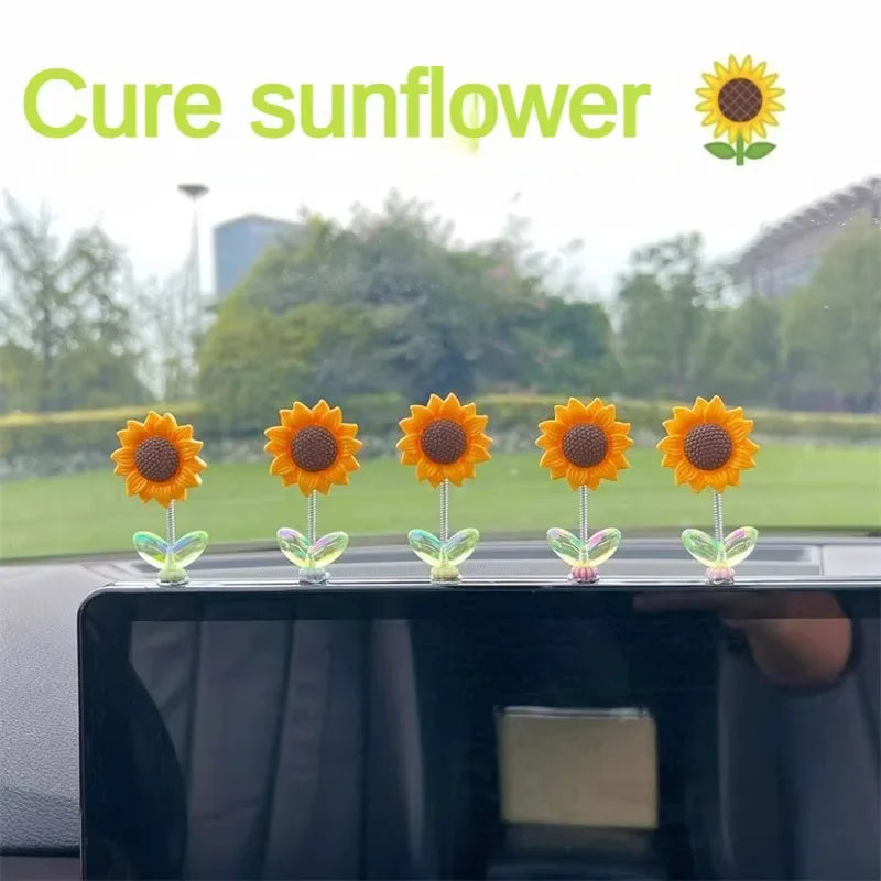 Cinq ornements de tournesols en verre avec des pétales jaunes et des tiges vertes sur une surface noire.