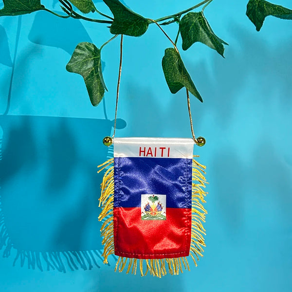A hanging flag of Haiti featuring the national colors and coat of arms, suspended by a thin cord.