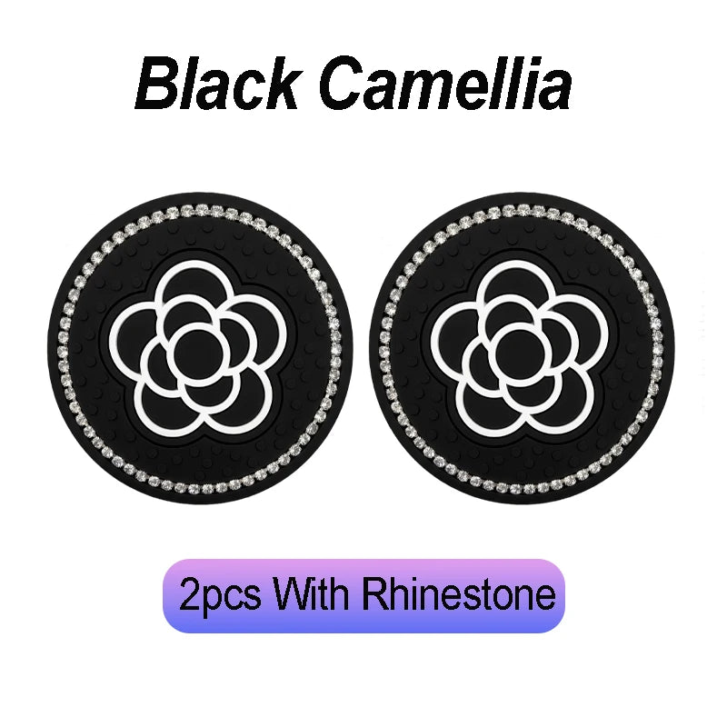 Two black camellia-themed coasters with rhinestone borders