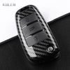 A black carbon fiber car key case cover with three visible key slots resting on a dark surface.